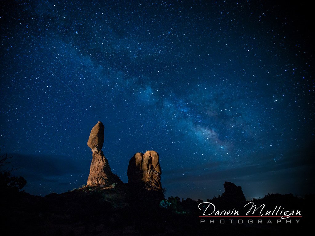 Spassing cars light up Balanced Rock, Milky Way Galaxy, Arches National Park, Utah